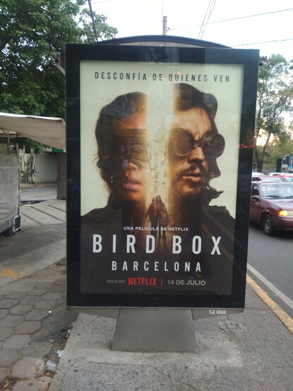 el letrero de una nueva serie de Netflix: BIRD BOX, que dice "desconfía de quienes ven" y saca a dos sujetos con los ojos vendados viendo con miedo en direcciones contrarias. En Medio, formando un halo de luz, se encuentran ellos dos con un niño, todos con los ojos vendados, caminando por una calle. 

La película es de Netflix. 