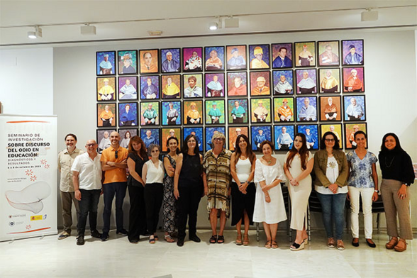 Se ve a 14 personas que participaron en el seminario sobre el discurso del odio, muchas de ellas del grupo INFOBISOC. Detrás de las personas hay fotos de gente de la universidad de Málaga con colores vivos