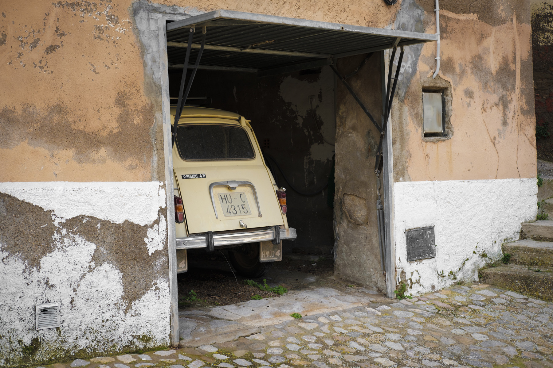 Un coche antiguo asoma por la puerta de un garaje abierto en una casa vieja de pueblo.