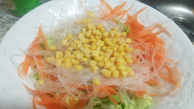 Foto de una fuente con ensalada china en la que se ve debajo las hojas de col china y sobre ellas, tiras de zanahoria, algas agar-agar y granos de maíz.