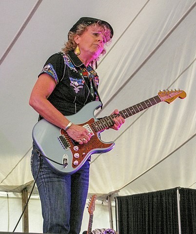 Una mujer de avanzada edad con gorra tocando una guitarra strat.