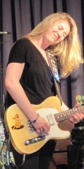 En el escenario una artista blanca y rubia tocando emocionada una telecaster con los ojos cerrados.