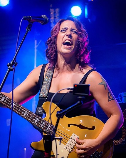 Artista blanca tocando un bajo para zurdos de cuerpo semiacústico con los ojos cerrados y la boca abierta

