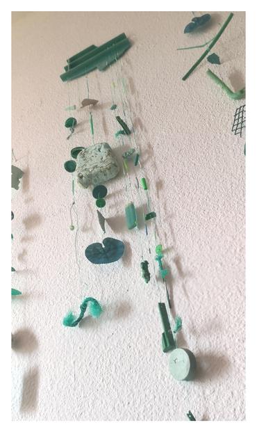 Otro ángulo del móvil principal visto desde abajo. Plásticos recogidos d la playa d tonos verdes. Palos d chupete, tapas, hojas plásticas, un auricular, etc. cuelgan atados a hebras d cuerdas d pesca. 