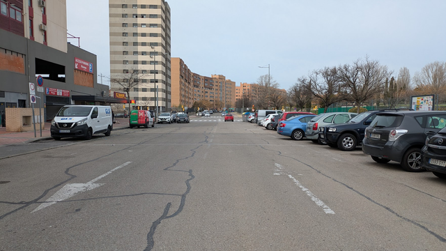 Calle desangelada. Una manta de asfalto mal conservada se extiende a lo ancho de 17 metros, parapetada lateralmente por dos barreras de vehículos estacionados. El grueso de la calle es carril, de más de 5 metros de ancho cada uno.