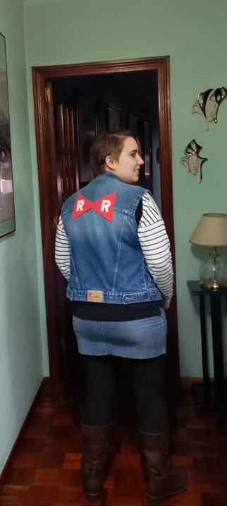 De espaldas. Se ve el logo de la Red Ribbon sobre la chaqueta vaquera. 