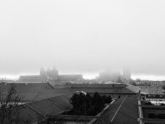 Imagen en blanco y negro del skyline de Salamanca con las Catedrales y la Clerecía en el centro de la imagen, envueltas en niebla.