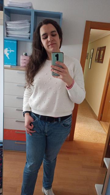 Selfie de mi reflejo en el espejo.Visto un jersey blanco y pantalones azules, y mi pelo cae sobre mi pecho. La pose es confiada.