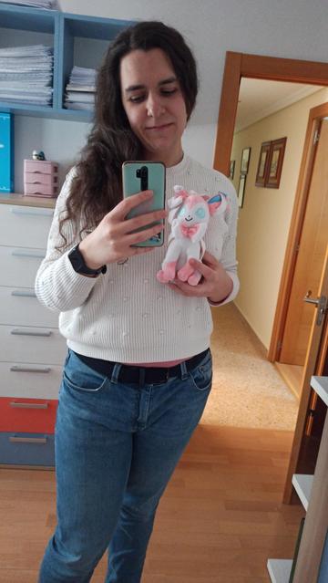 Selfie de mi reflejo en el espejo.Visto un jersey blanco y pantalones azules, y mi pelo cae sobre mi pecho. Llevo un peluche de Sylveon en la mano izquierda
